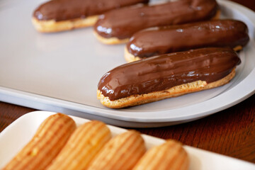 French dessert eclairs or profiteroles with dark chocolate glaze. Pastry cakes with cream and topping. Soft selective focus.