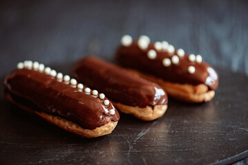 French dessert eclairs or profiteroles with dark chocolate glaze and drops. Pastry cakes with cream and topping. Soft selective focus.