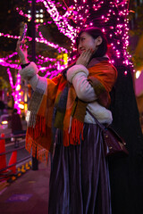 Fototapeta premium A Japanese girl shooting selfie at night illuminated street in Shibuya
