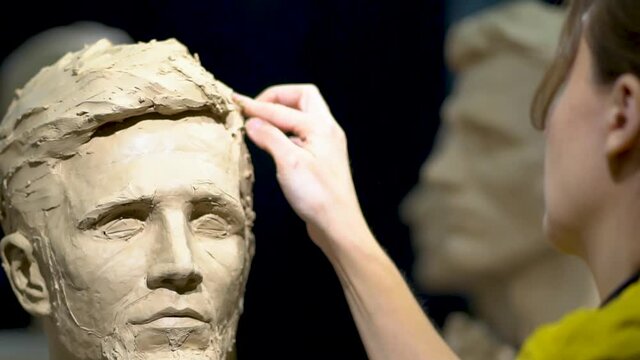 Woman sculptor at work on a sculpture of a human head.