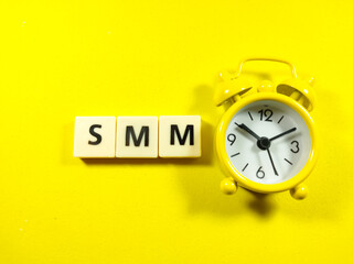 Business concept.Yellow clock and scrabble letters with text SSM (Social Media Marketing) on yellowbackground.