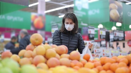 Young woman in a protective mask in the supermarket chooses fruit and puts it in a plastic bag. Fruit in the supermarket. Shopping in a store or market.
