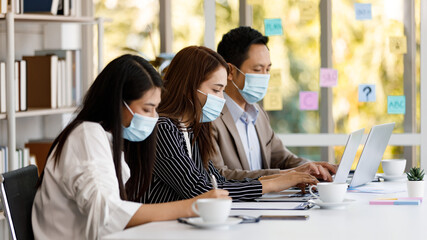 coronavirus prevention in the office. Group of Asian businesspeople wearing face masks and wearing formal clothes working at the office table. Covid-19 new normal lifestyle concept