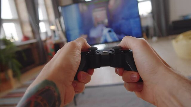 POV of man with tattoo on arm using black console controller as playing shooter video game on TV at home