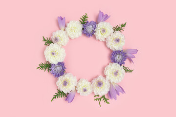 Wreath made of dahlia and colchicum flowers on a pink pastel background. Round frame with copyspace.