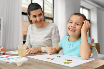 family, motherhood and leisure concept - happy smiling mother spending time with her little daughter drawing or painting wooden chipboard items with colors at home