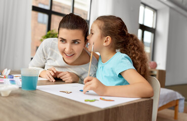 family, motherhood and leisure concept - happy smiling mother spending time with her little daughter drawing or painting wooden chipboard items with colors at home