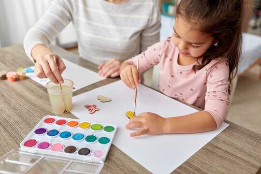 family, motherhood and leisure concept - mother spending time with her little daughter with colors painting chipboard items at home