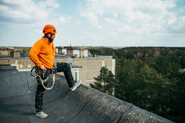 Tired and dirty industrial climber with beard have rest on the roof after work and enjoying the sun. Worker outside. Grey buildings