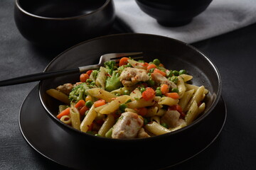 Pasta salad with baked vegetables and fried pieces of chicken breast . Penne pasta with broccoli, beans and carrots.