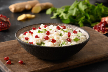 Curd Rice with pomegranate, cilantro, mustard seeds, ginger on a dark background. Indian South cuisine. Close up.