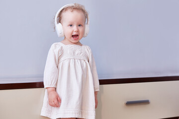 Little girl sings a song in her headphones. Light background with space for text