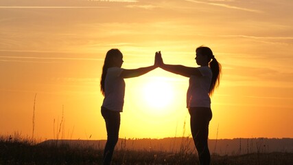 Mom and daughter touched their palms to each other, hands over a beautiful sunset. Happy family mom and daughter in field in sun. concept of a happy family of children and childhood. Mommy and kid