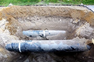 An open trench in a city street with pipes visible. Sewerage and water supply repair