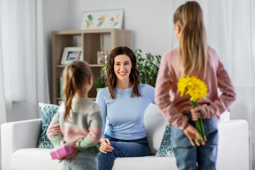 people, family and holidays concept - two daughters giving flowers and birthday present to happy mother at home