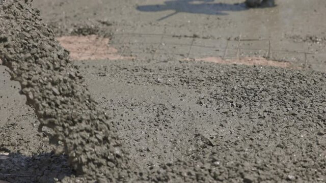Concrete flowing and pouring from mixer cement truck pours liquid concrete in works road at construction site.