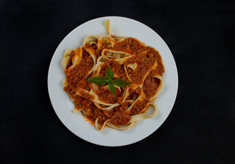 Pasta Tagliatelle with bolognese sauce and basil leaves. Typical Italian pasta. Top view photo with black textured background.