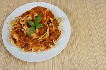 Tasty Pasta with bolognese sauce and basil leaves. Pasta served on a plate on a bamboo mat. Italian gastronomy photography. Photo with space for text on the right.