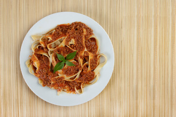Tasty Pasta with bolognese sauce and basil leaves. Italian handmade pasta served on a bamboo mat in the background. Top view photo with space for text.