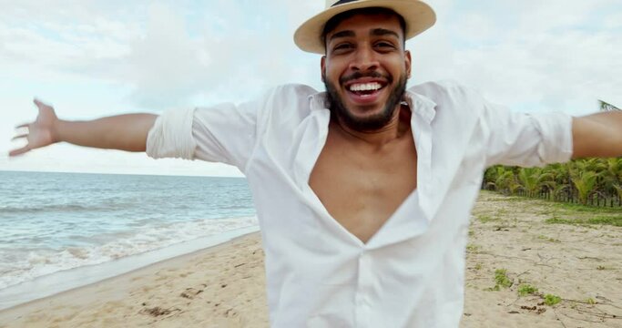 Friendly young Latin American man inviting to come to Brazil, confident and smiling making a gesture with his hand, being positive and friendly. Beach from Brazil. 6K.