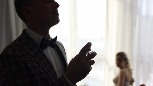 Groom splits the perfume or deodorant on hisself near bride . Wedding day. Slow motion. Well dressed handsome businessman using perfume from a bottle