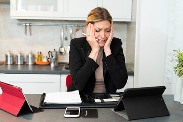 Worried business woman looks at the tablet.
Blond woman working from home is scared after messing...