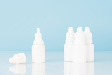 Eye drop or ear drop bottles on light blue background. Blank white plastic container for fluid. Pharmaceutical packaging product.