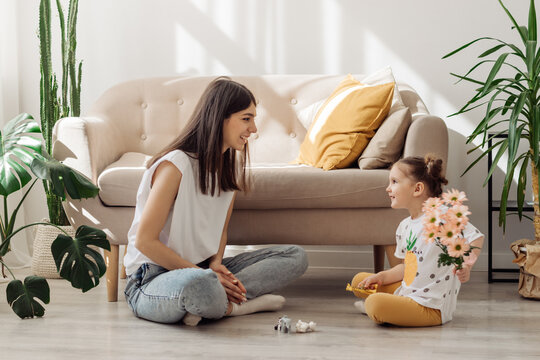 A dark-haired young mixed-race woman playing on the floor with her little daughter.The girl giving her mother flowers.Home interior design.Time together.Family concept and Mother's Day concept.