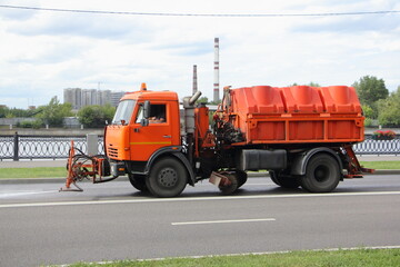 Modern Russian orange watering truck pours asphalt road, street washing in Moscow, city improvement by municipal services on a sunny summer day