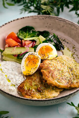 Side view on zucchini fritters with eggs sauces and vegetables