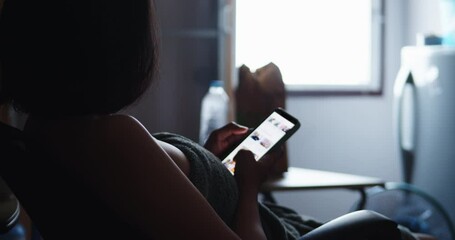 A lonely poor working-age woman rented an apartment, kept in a narrow room, dimly lit, there was light from the window, fast food on the table, wearing a towel, watch social media on a mobile phone.
