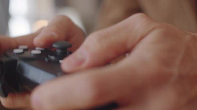 Close up shot of hands of unrecognizable man using black wireless controller while playing console game