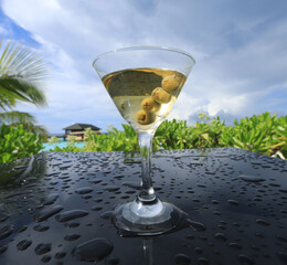 glass with martini cocktail with olives on the table outdoors in summer
