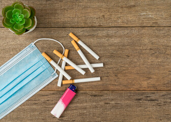 Cigarette, gas lighter and face mask on wooden board background. Copy space.