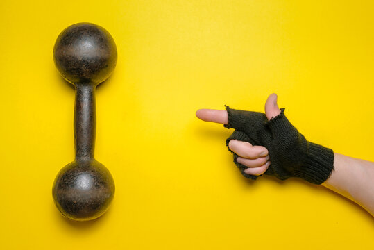 Male Hand In The Black Glove Is Pointing On The Old Dumbbell On A Yellow Background.