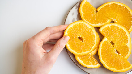 Hand taking a slice of orange from the plate on the table. Orange slice at the hand. Juicy orange on a gray plate