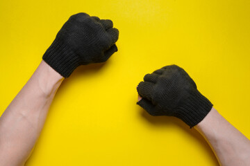 A male hands in the black gardening glove with a clenched fist on the yellow flat lay background.