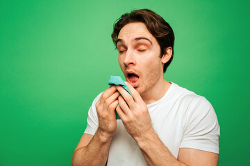 Young man looks sick and has running nose, isolated on green background