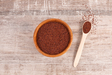 Red quinoa seeds in wooden bowl and spoon on wooden background.