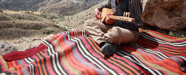 Fototapeta na wymiar Man playing traditional Turkish musical instrument (Saz). Woven rugs.