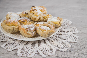 Close-up of traditional Portuguese homemade puff pastry with egg cream on a light table with a lace napkin. Dessert Pasteis de nata.
