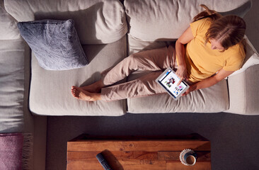 Obraz premium Overhead Shot Of Woman Relaxing On Sofa Browsing Or Streaming Movie On Digital Tablet