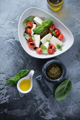 Caprese salad with mozzarella, red cherry tomatoes, green basil and basil pesto sauce, top view on a grey concrete background, vertical shot