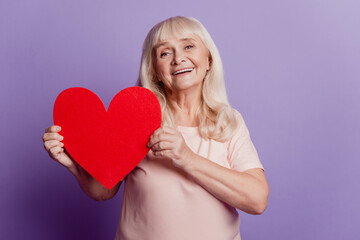 Photo of smiling elderly woman hold big valentine heart card isolated on violet background