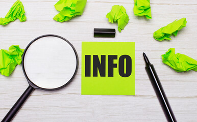 The word INFO written on a green sticky note next to a magnifying glass and a black marker on a...