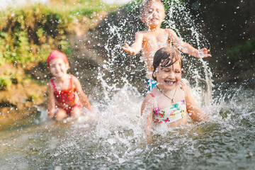 Happy summertime, healthy childhood concept. Caucasian children playing, splashing, jumping and having fun in a river in summer. Selective focus on one kid. Horizontal shot.