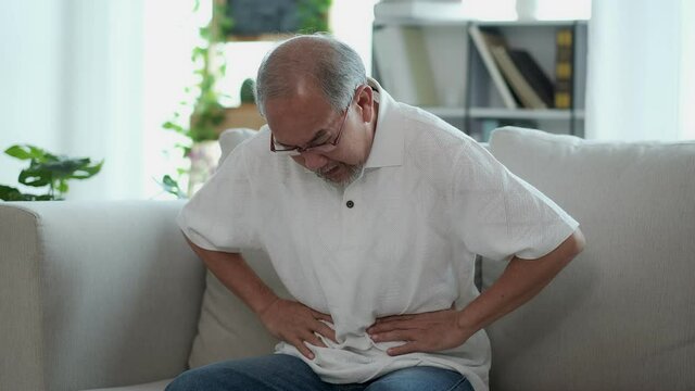 The Asian elderly man sit on sofa has a stomach ache. Caused by illness due to food poisoning