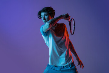 Young caucasian man playing tennis isolated on purple-blue studio background in neon, action and motion concept