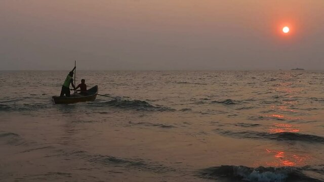 Traditional fishermen guiding their boats through tides and making their way to ocean during sunset, Malvan, Maharashtra