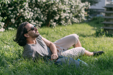 Fototapeta premium A man sits on the grass in a blooming park in a big city.